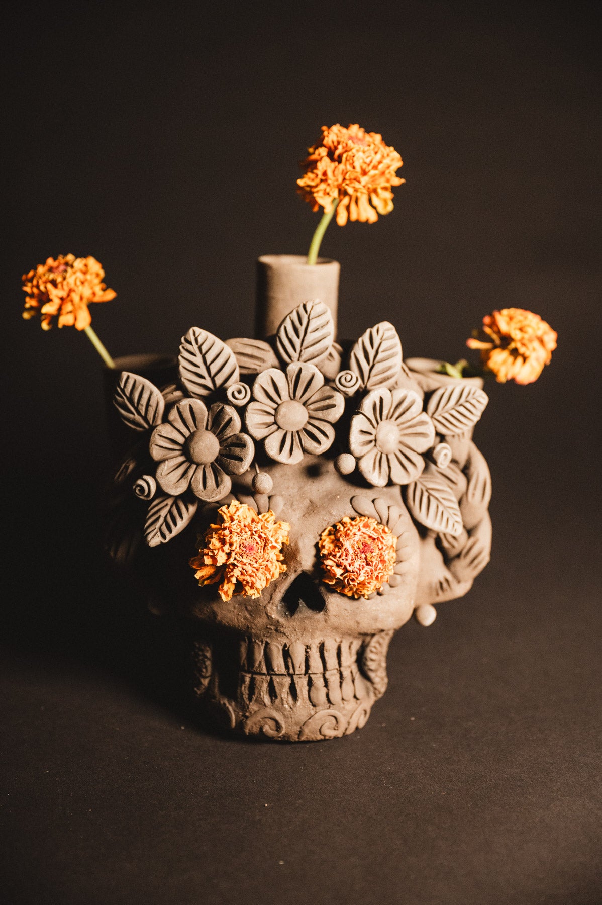 Ceramic skull vase with floral designs and orange flowers on a dark background