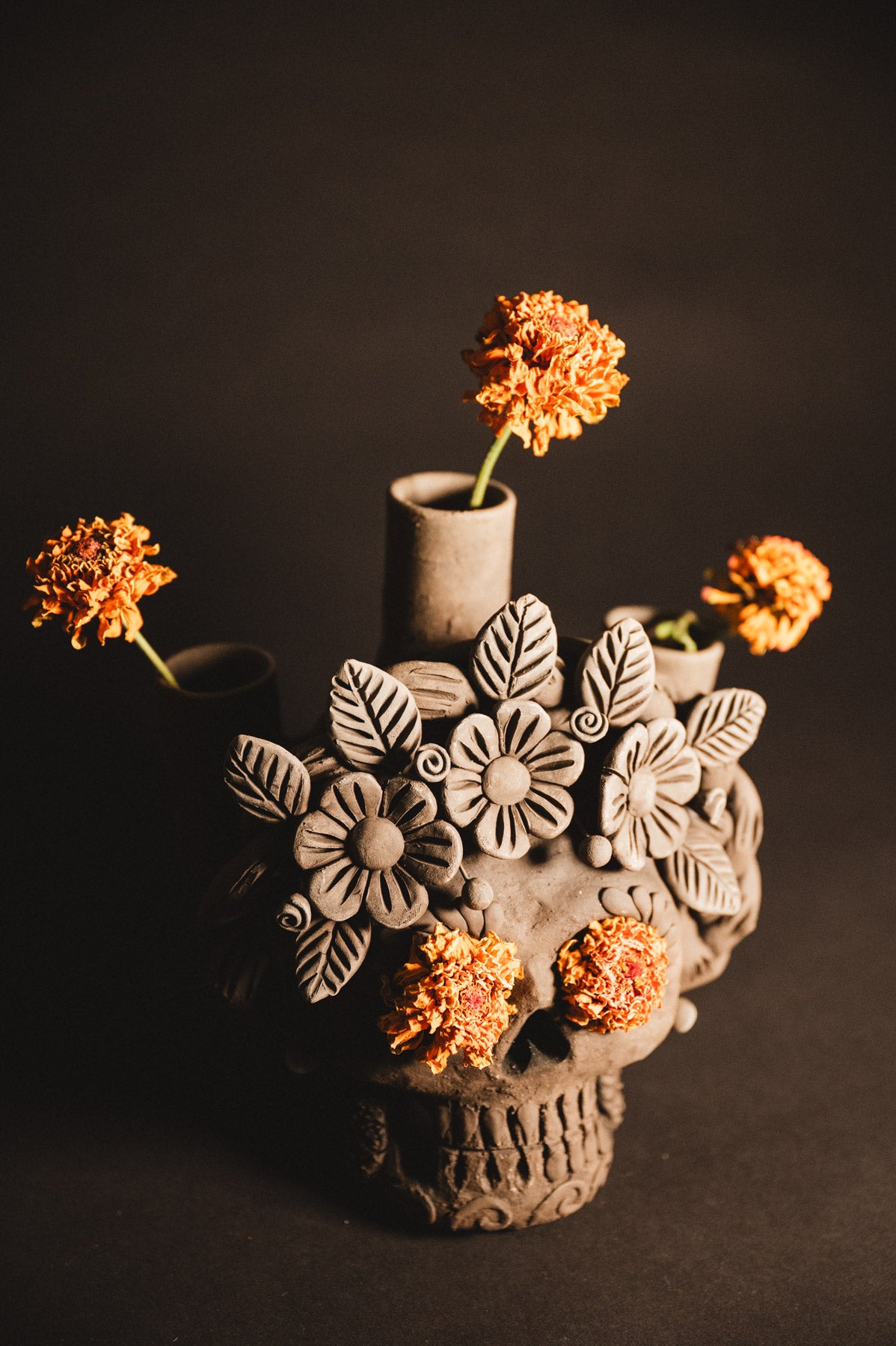Ceramic skull vase with floral designs and orange flowers on a dark background