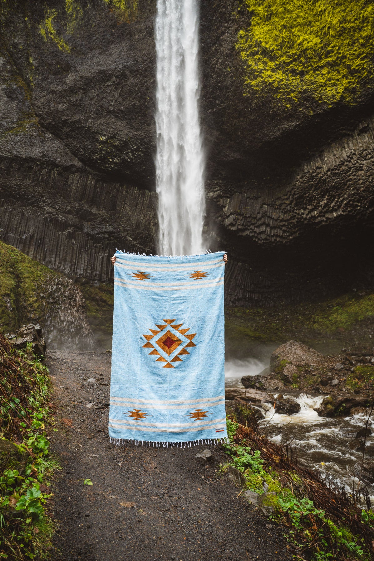 Blue patterned rug draped over a natural rock formation with water flowing through.