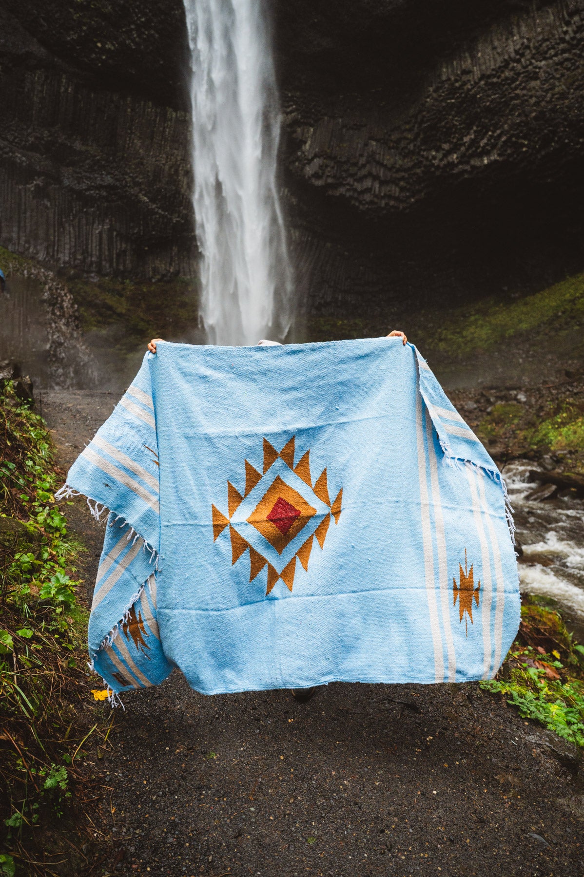 Blue blanket with a geometric pattern draped over a chair in front of a waterfall.