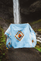 Blue blanket with a geometric pattern draped over a chair in front of a waterfall.