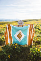 Person sitting on a blanket with a colorful pattern in a field of wildflowers