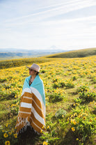 Person wrapped in a striped blanket standing in a field of yellow flowers