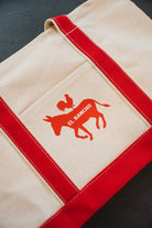 Beige bag with red accents and a logo on a dark surface