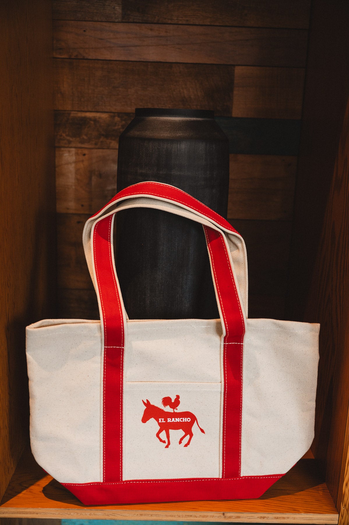 White tote bag with red straps and logo on a wooden surface