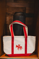 White tote bag with red straps and logo on a wooden surface