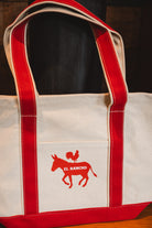 White tote bag with red handles and a logo featuring a donkey and rooster on a dark background