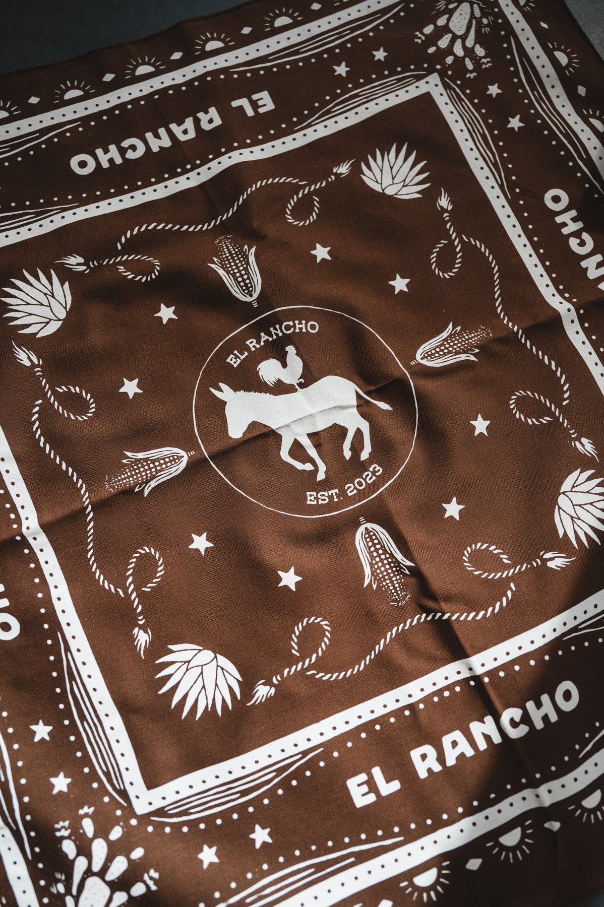 Brown bandana with white patterns and 'El Rancho' branding