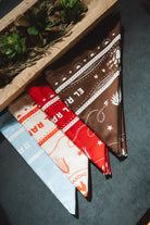 Two fabric swatches, one red and white patterned and one brown with white designs, on a dark surface.