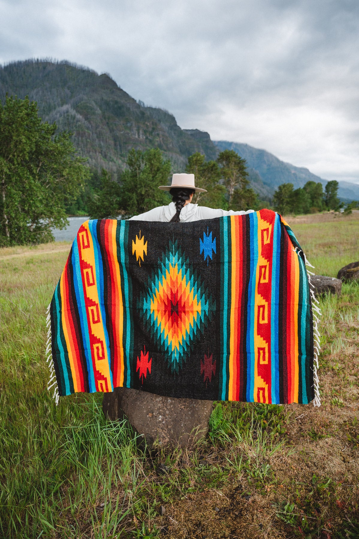 Mexican woman holding multicolored handwoven mexican blanket with greca designs