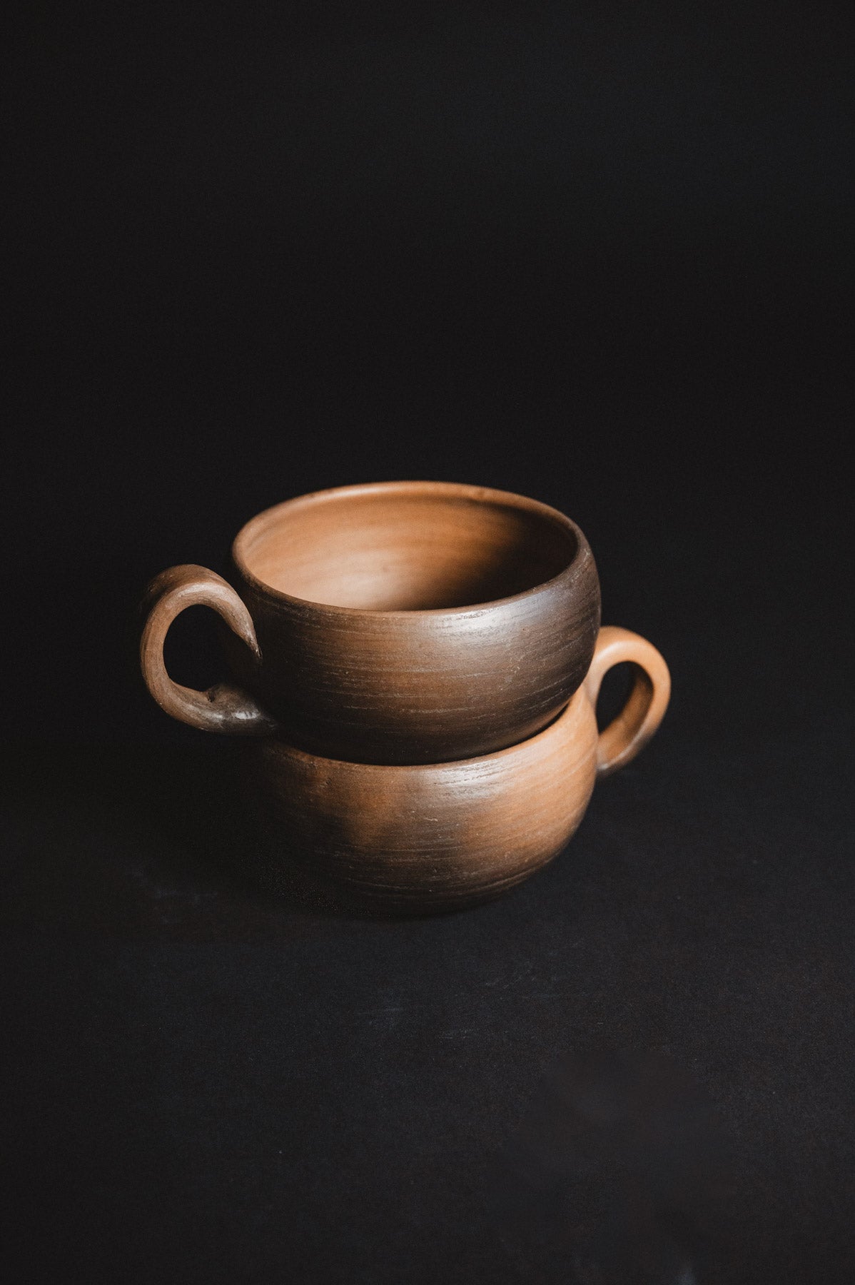 Two brown ceramic cups stacked on a black background