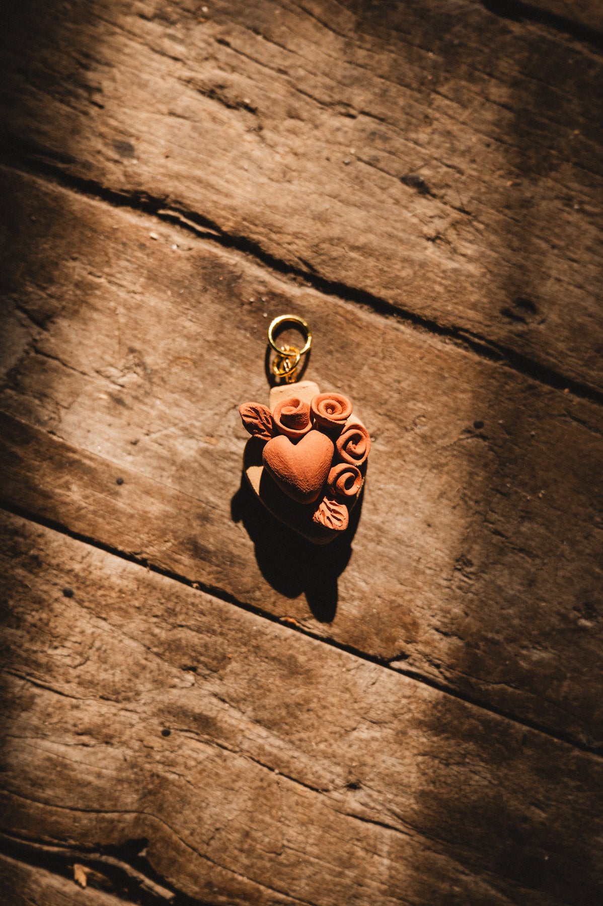 Terra cotta heart-shaped pendant with floral designs on a wooden surface