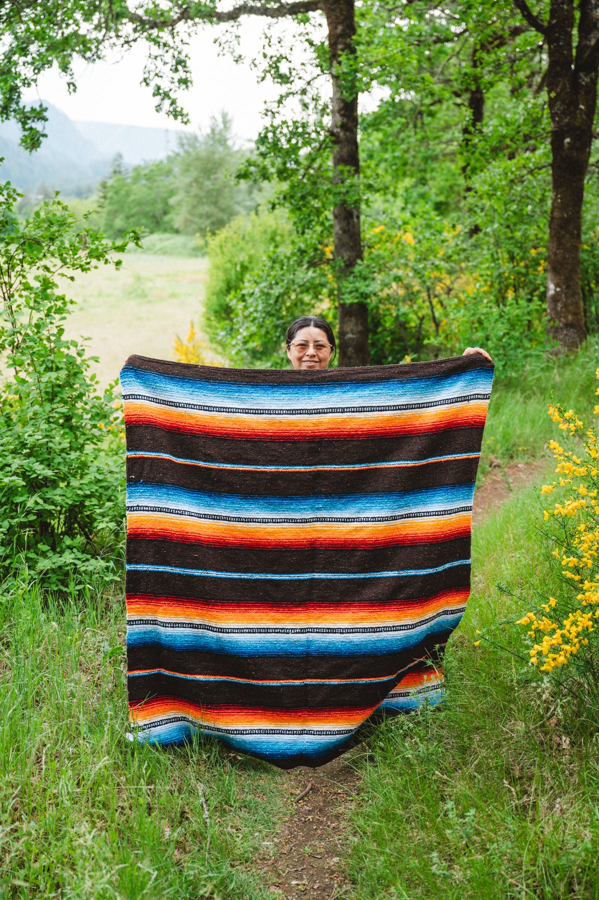 Woman holding handwoven black saltillo blanket in the forest