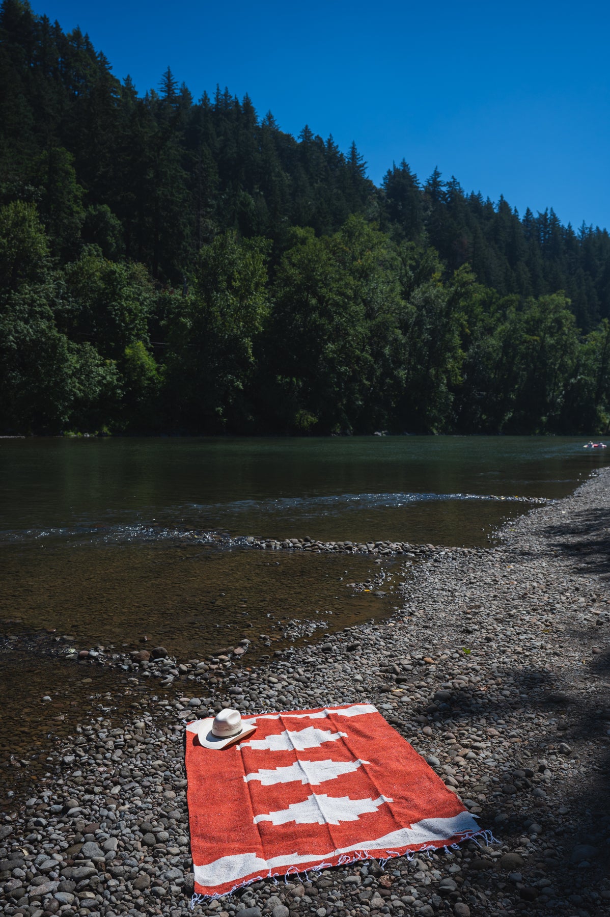 Red and white handowoven mexican blanket laying on a rocky riverbank