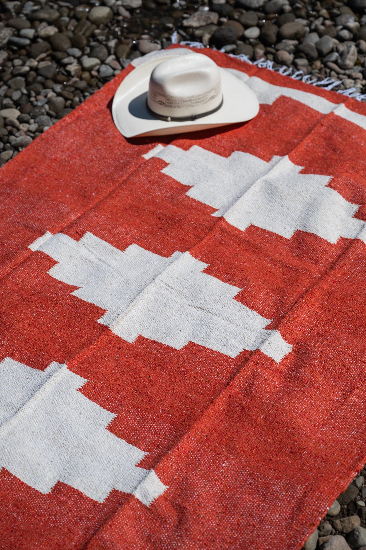 Red and white handowoven mexican blanket laying on a rocky riverbank