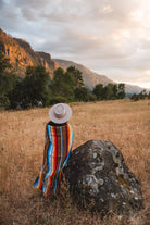 Woman standing next to rock in field wrapped in handwoven brown saltillo blanket