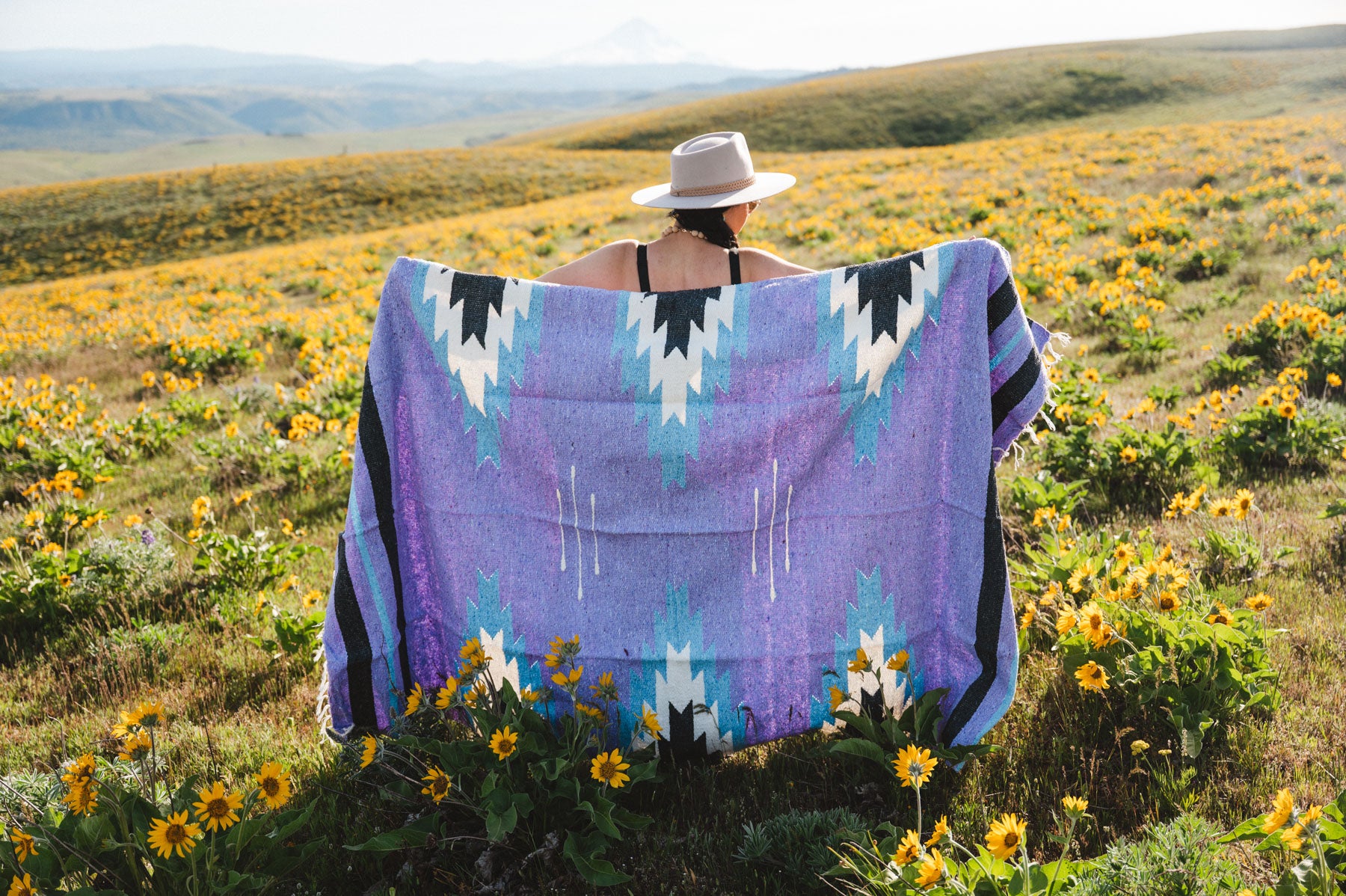 Person standing in a field of wildflowers wearing a colorful patterned blanket
