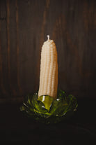 An off-white corn cob pillar candle standing upright in a translucent green glass holder against a dark wooden background.