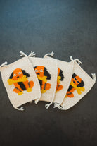 Four cream-colored woven drawstring pouches with a colorful embroidered dog motif in orange, black, and yellow, arranged on a dark gray background.