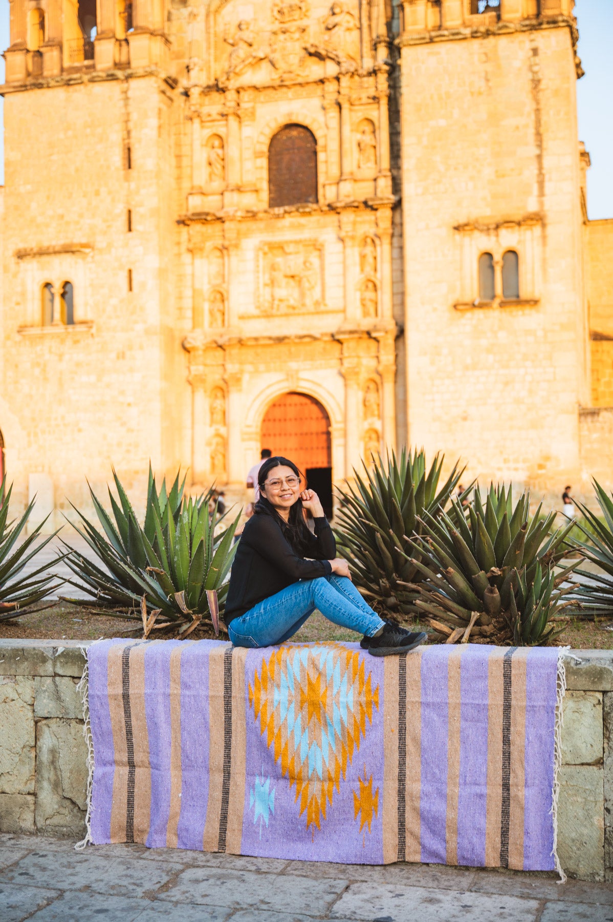 Santo Domingo Oaxaca and a girl sitting on a handwoven mexican blanket in front of it