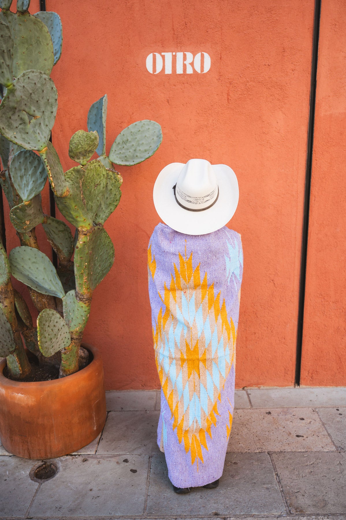 Girl wrapped in lavender handwoven mexican blanket in front of orange wall next to catctus