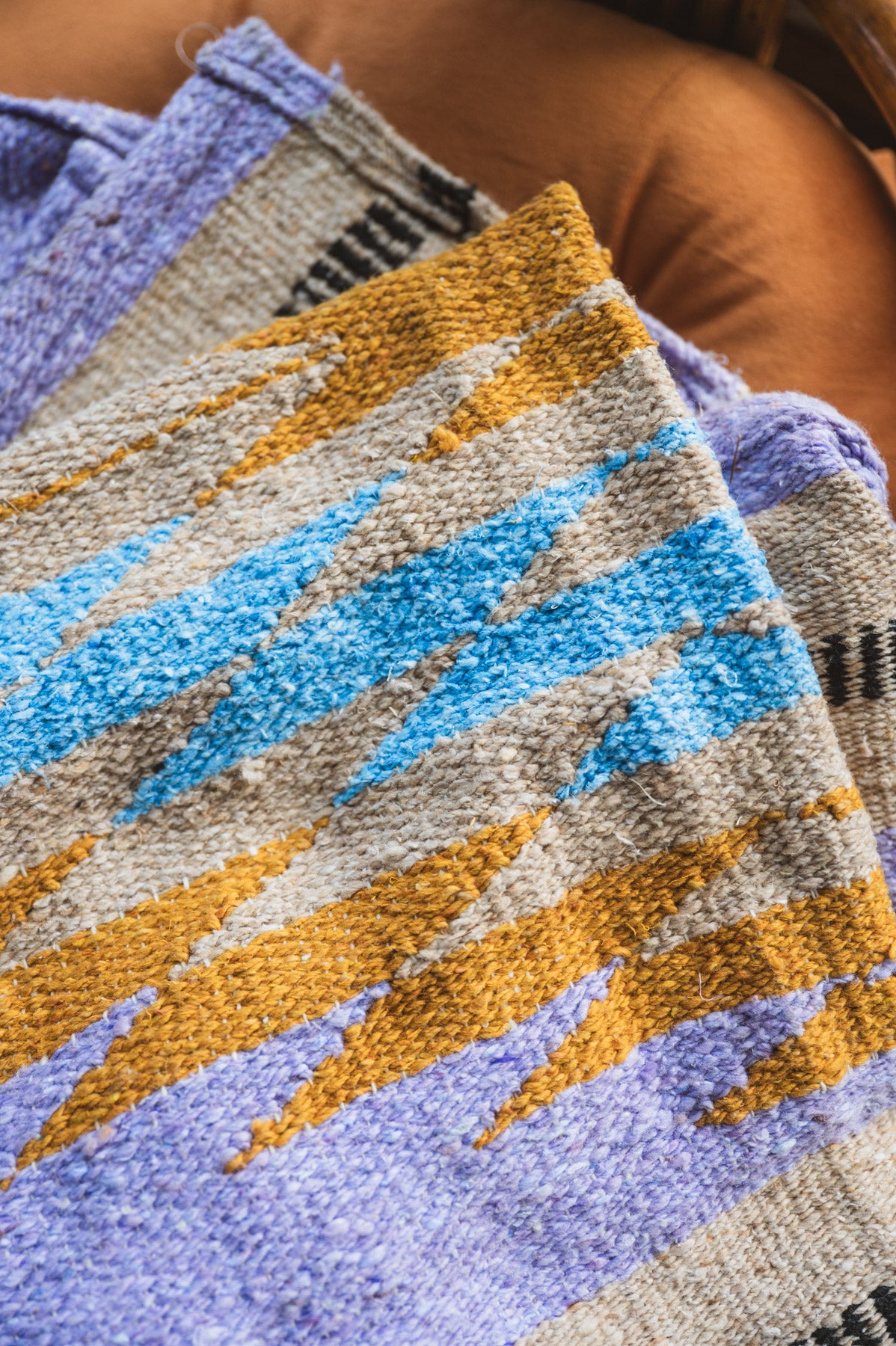Textured fabric with geometric pattern in blue, orange, and gray on a brown surface.