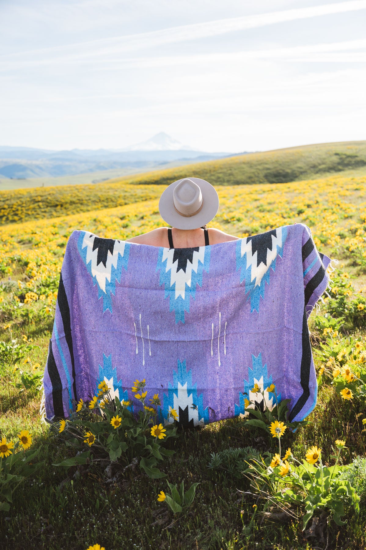 Person wearing a purple patterned towel in a field with wildflowers