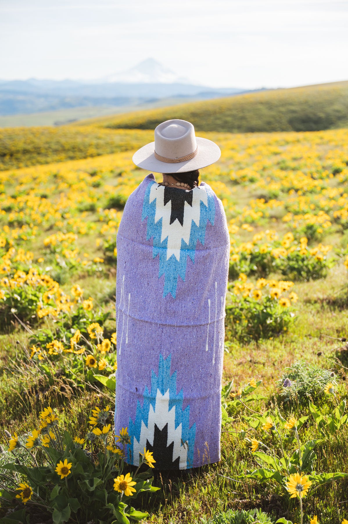 Person wrapped in a patterned blanket standing in a field of wildflowers