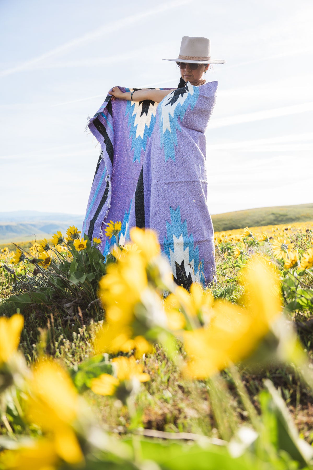 Person holding a colorful patterned blanket in a field of yellow flowers