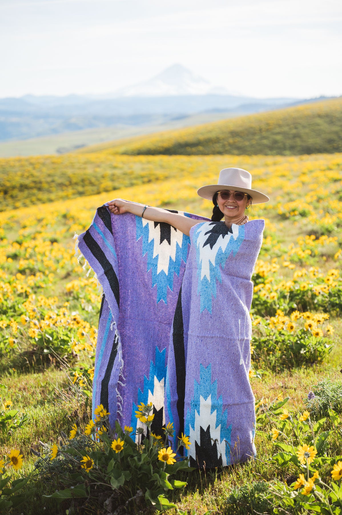 Woman holding a colorful patterned blanket in a field of wildflowers with mountains in the background