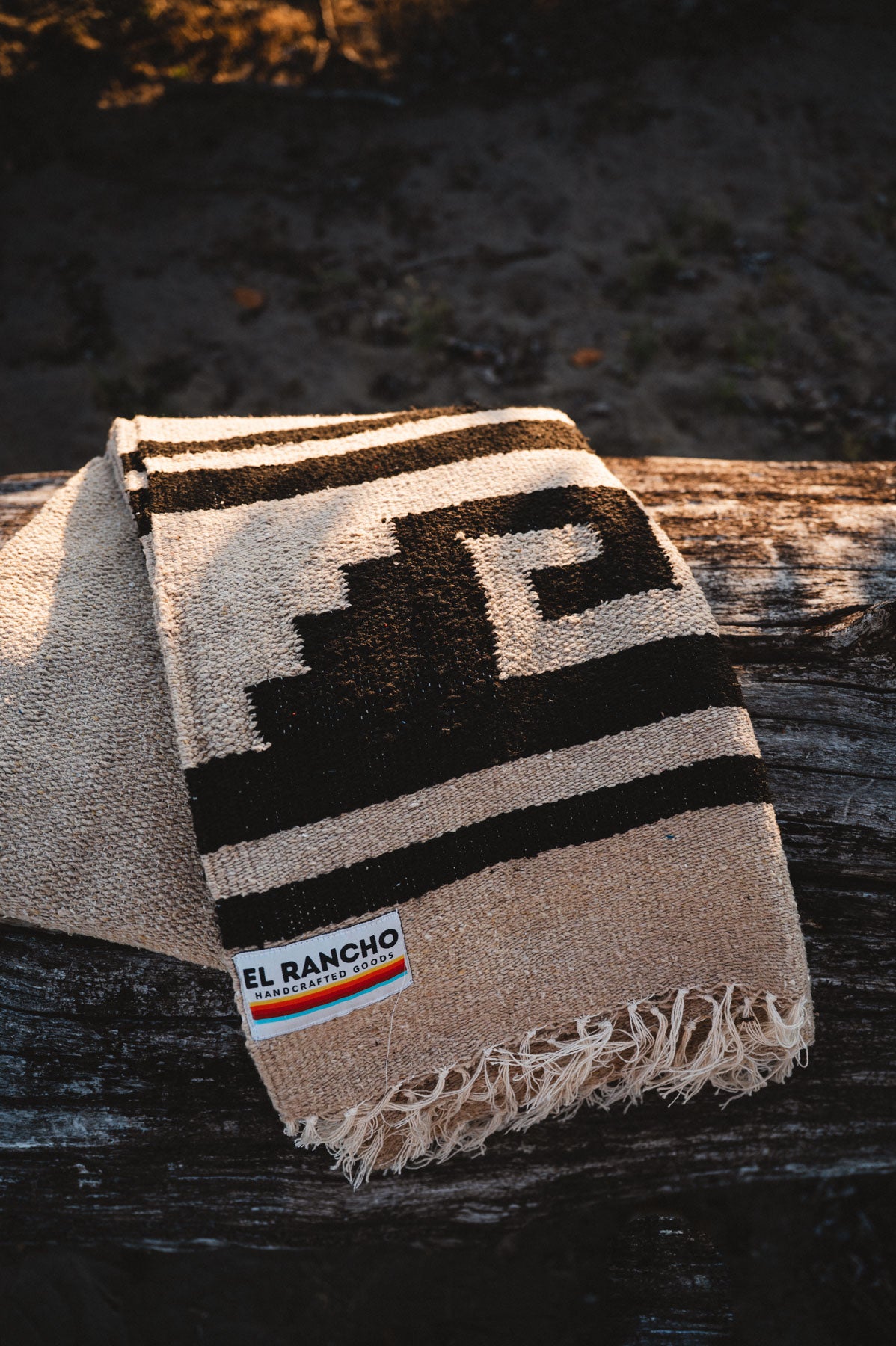 Beige and brown patterned blanket with 'El Rancho' logo on a wooden surface