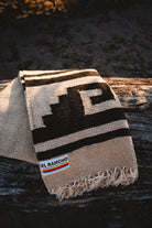 Beige and brown patterned blanket with 'El Rancho' logo on a wooden surface
