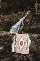 Person holding a patterned blanket in front of a waterfall