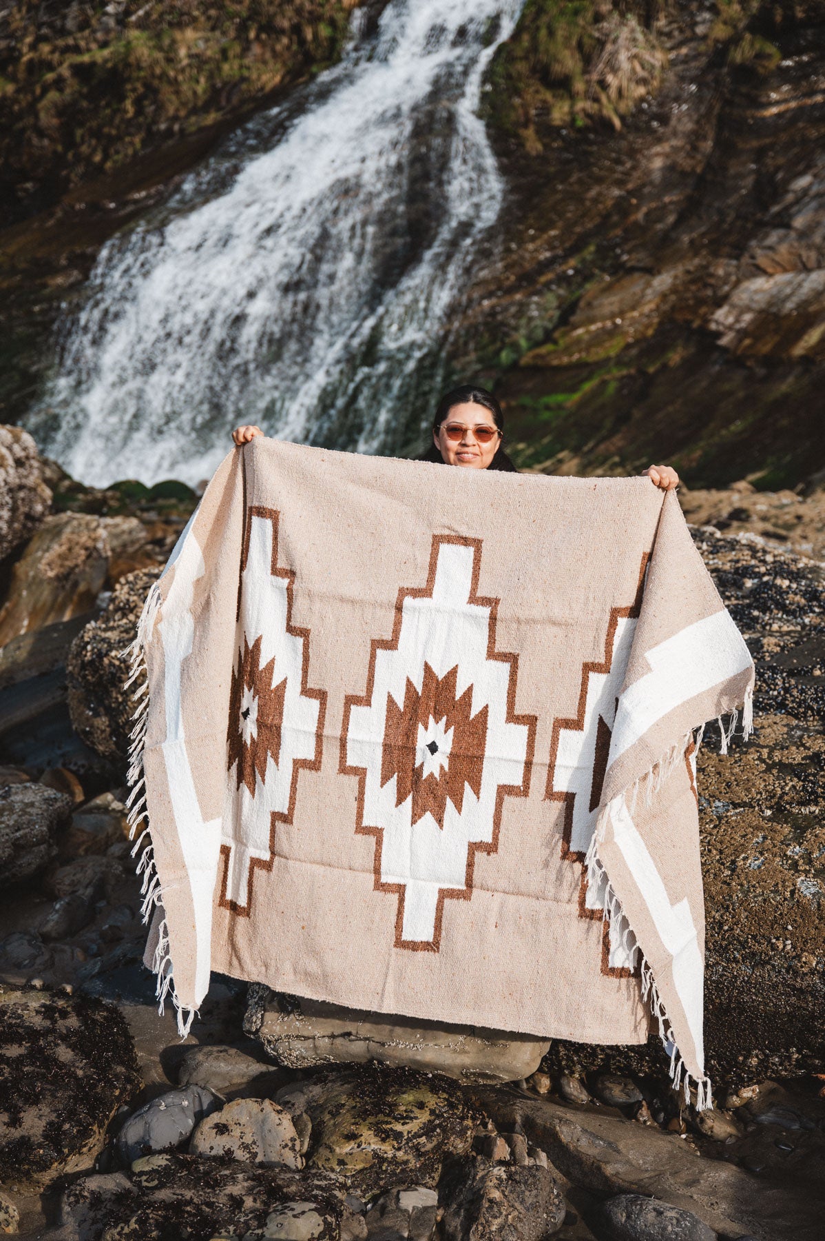 Person holding a patterned blanket in front of a waterfall