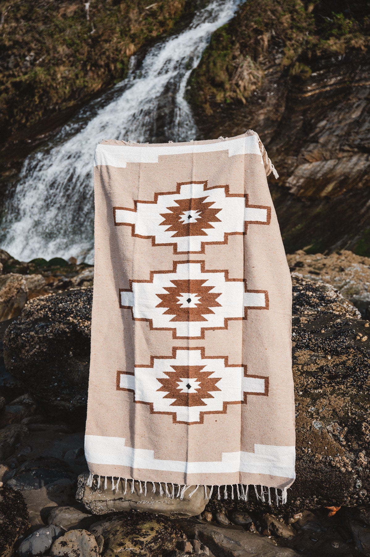 Beige blanket with geometric patterns draped over a rock by a waterfall