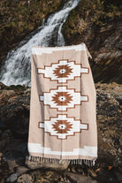 Beige blanket with geometric patterns draped over a rock by a waterfall