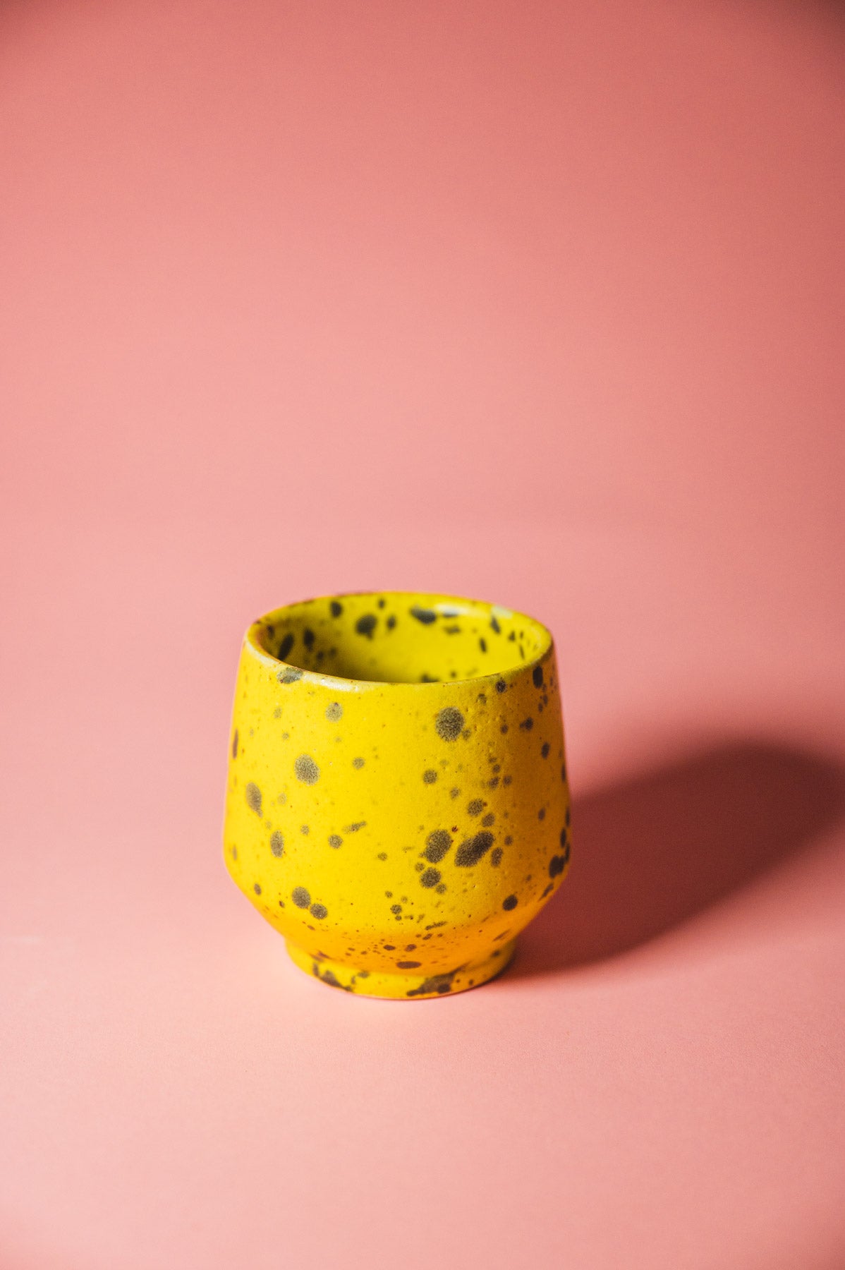 Yellow ceramic cup with black speckles on a pink background
