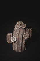 A sculptural cactus-shaped ceramic vase with textured vertical ridges and five raised flower motifs, shown on a solid black background.