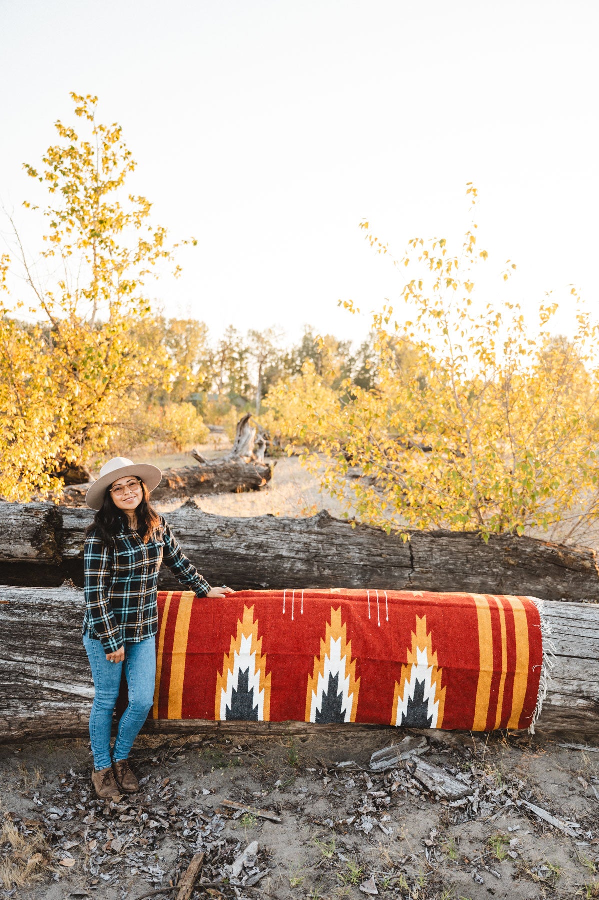 Person sitting on a large relampago patterned mexican blanket outdoors with trees and logs in the background
