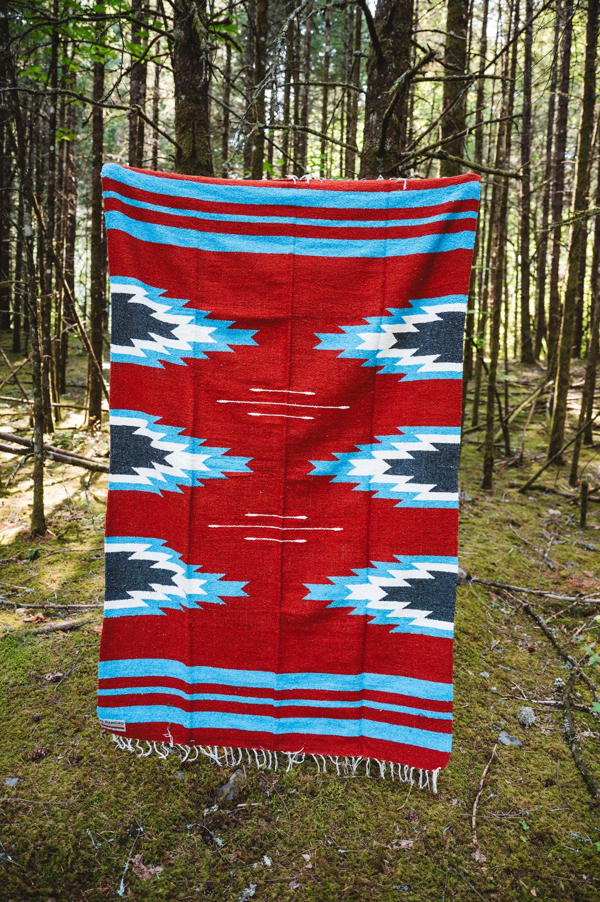 Red and blue relampago patterned handwoven mexican blanket in a forest background