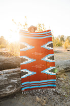 Person holding a large relampago patterned mexican blanket outdoors with trees and logs in the background