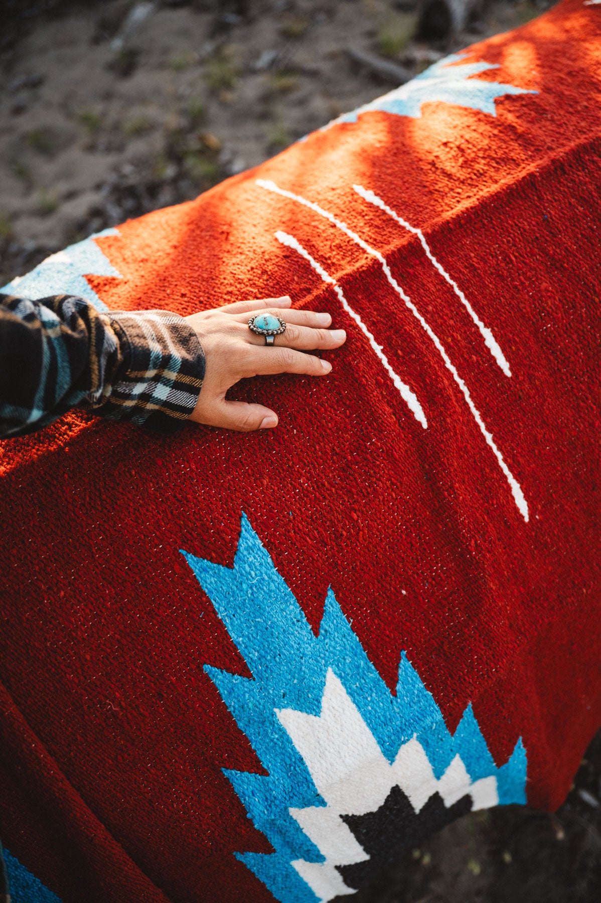 Hand with a ring on a red patterned fabric with blue and white designs.