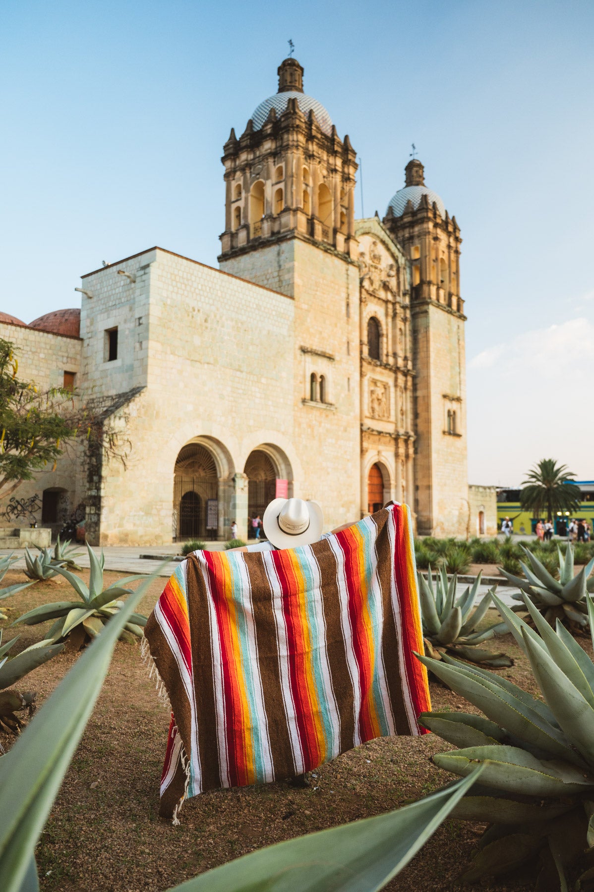 Santo Domingo Church Oaxaca and a girl standing with a handwoven mexican blanket in front of it