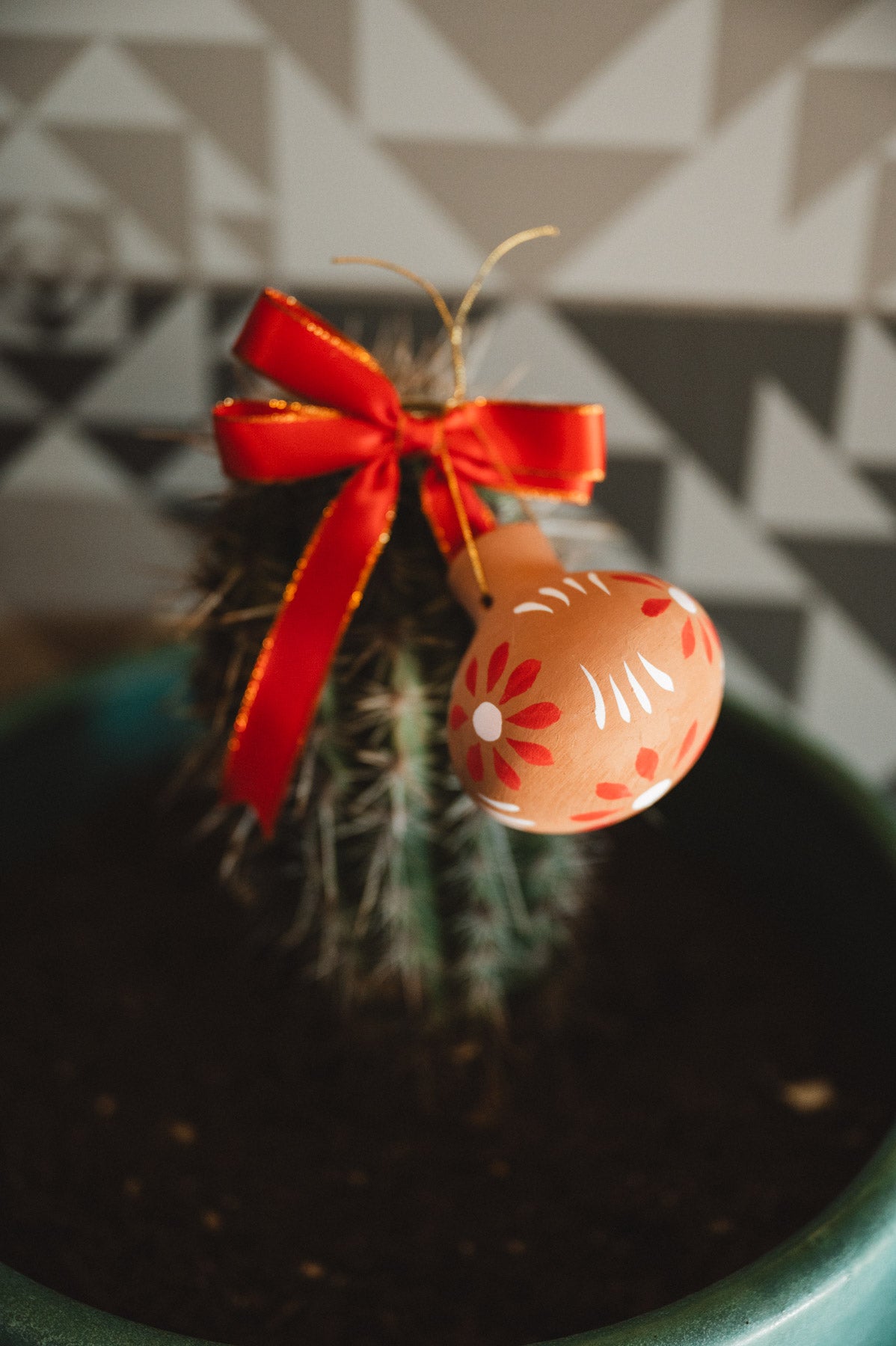 Decorative oval christmas decoration with floral pattern and red ribbon hanging on a cactus plant.
