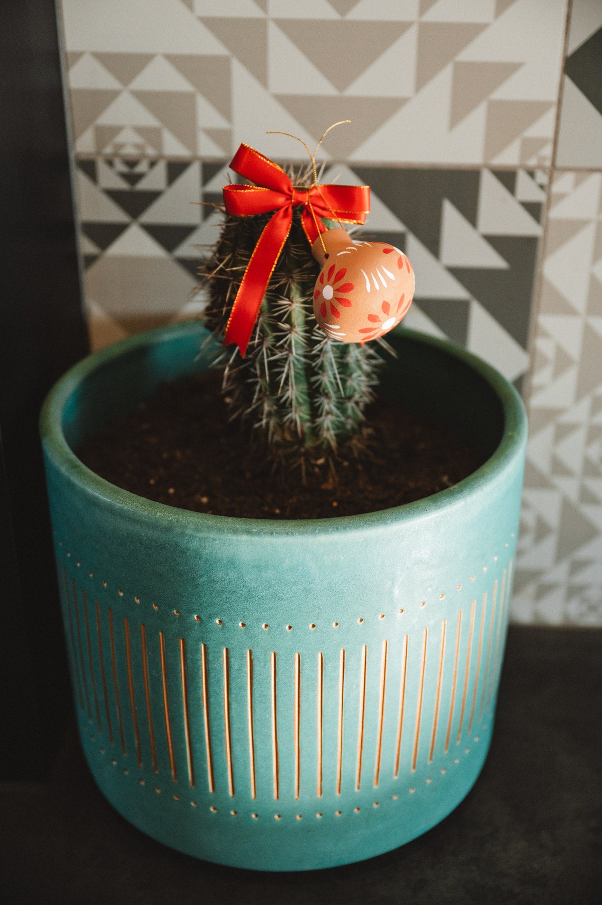 Decorative oval christmas decoration with floral pattern and red ribbon hanging on a cactus plant.