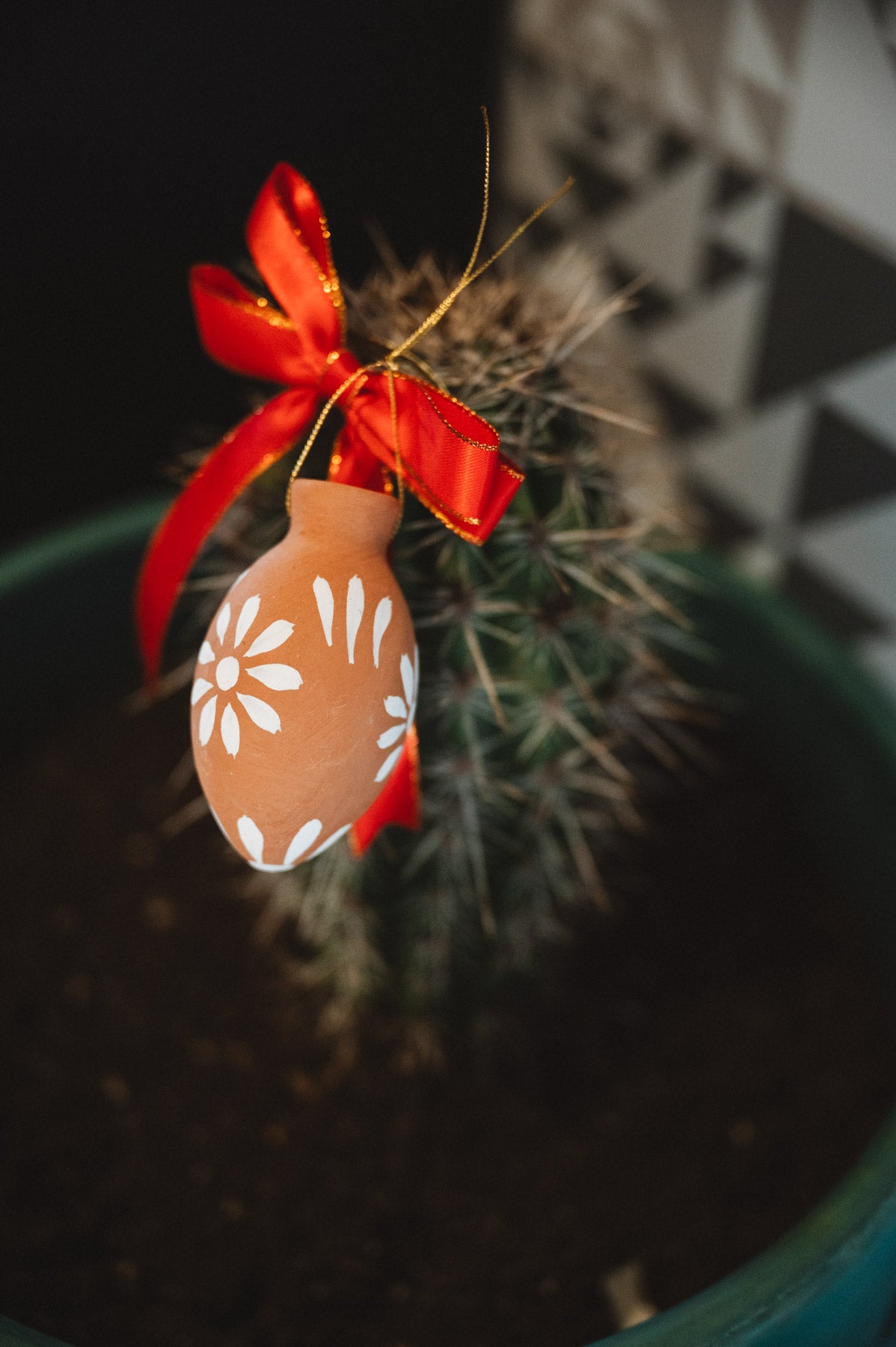 Decorative oval christmas decoration with floral pattern and red ribbon hanging on a cactus plant.