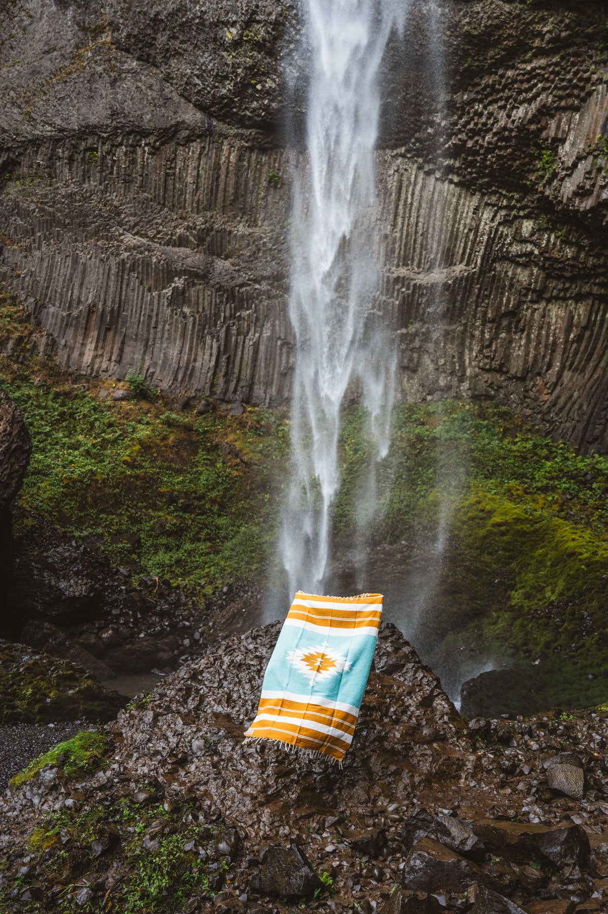turquoise and gold mexican blanket in front of a waterfall