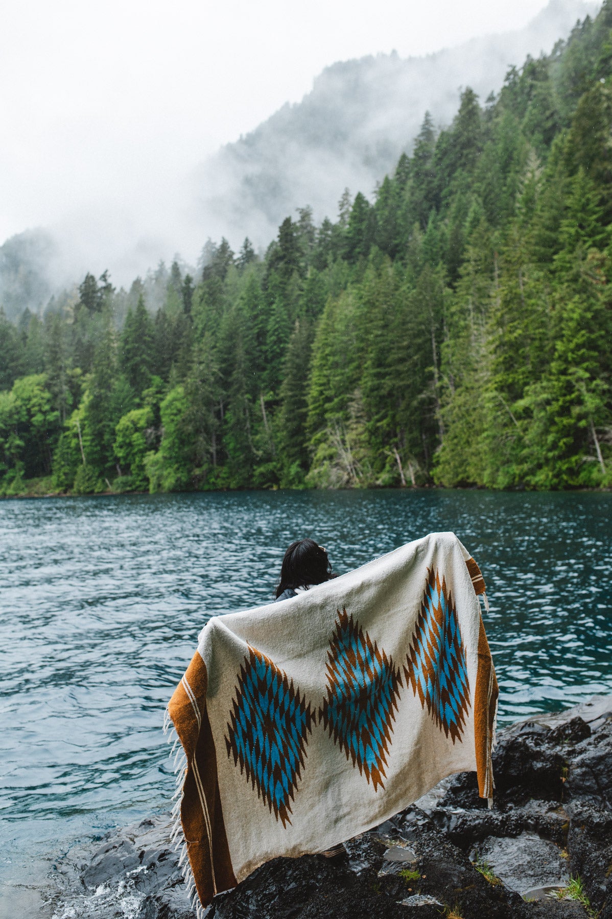 Woman in the olympic peninsula PNW wrapped in a turquoise and gold handwoven mexican diamond blanket