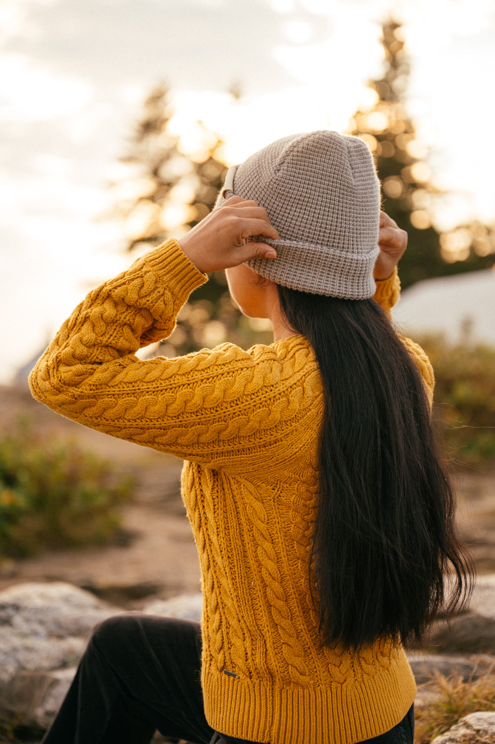 Girl putting on a grey waffle beanie at sunset