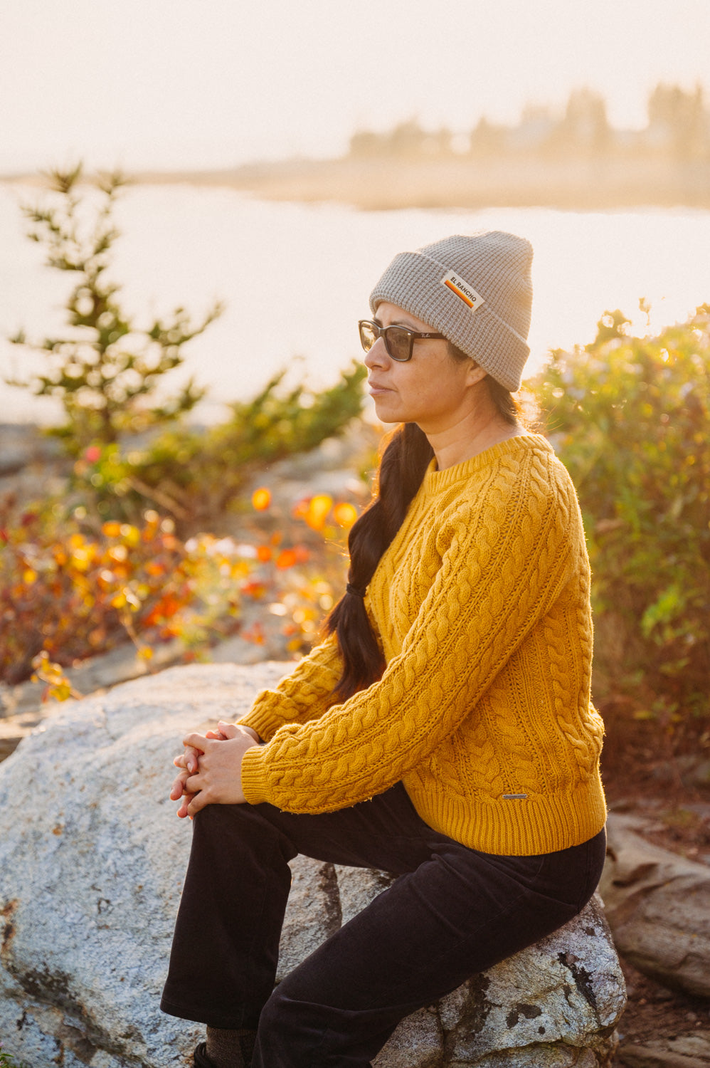 Girl wearing a grey waffle and gold sweater beanie at sunset